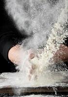 chef in black uniform sprinkles white wheat flour in different directions photo