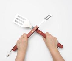 espátula de metal y tenedor con mango de madera para un picnic en una mano femenina con uñas pintadas de rojo sobre un fondo blanco foto