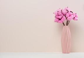 Pink ceramic vase with rose cotton bouquet on white table photo