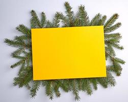 fondo de felicitación de navidad con una hoja amarilla vacía y ramas verdes foto