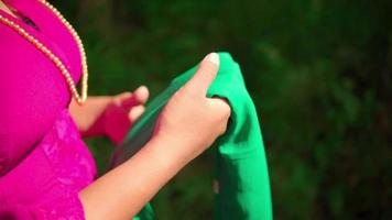Asian woman walking through the forest while holding a green scarf in her hands in a pink dress and makeup video