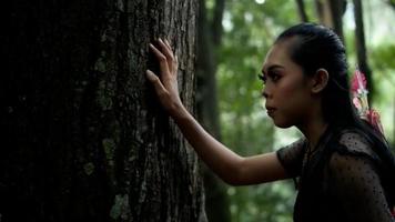 A women fighter with long black hair and an arrow on her back running to the big tree in the forest with a tired body and shortness of breath video