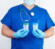 doctor in blue uniform and latex gloves is holding an empty plastic container for taking urine samples photo