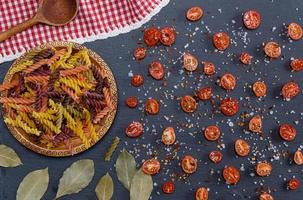 unprepared multi-colored pasta spiral made from wheat flour and cut into halves of cherry tomatoes photo