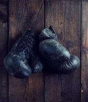 old shabby black leather boxing gloves hanging on a nail photo