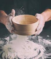 Chef in a black uniform holds in his hand a round wooden sieve photo