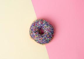 round baked donut with colored sugar sprinkles on a pink-yellow background photo