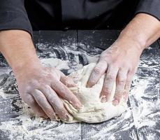 baker kneads white wheat flour dough on a black wooden table photo