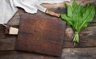 manojo de hojas verdes frescas de acedera y tabla de cortar marrón vieja foto