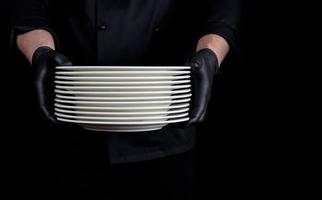 cook in black uniform holds in his hands a stack of round white empty plates photo