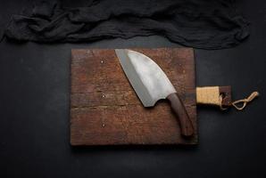 Rectangular empty wooden cutting board and kitchen knife on black table with gauze napkin, top view photo