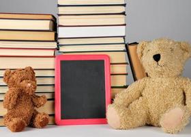 teddy bear and empty black board in red frame on the background of pile of books photo