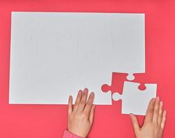 female hand puts white big puzzles on a pink background photo