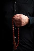 man in a black shirt holds a brown stone rosary in his left hand, low key photo