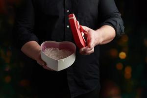 adult man in a black shirt holds a red cardboard box in the form of a heart with a bow photo