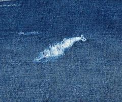 fragment of blue jeans fabric with a hole, full frame photo