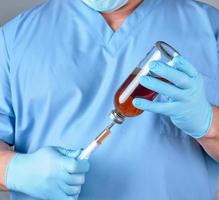 doctor in blue uniform holds a syringe and a glass bottle with injection photo