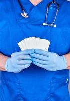 médico masculino con guantes de látex azules sostiene una tarjeta de visita de papel blanco en blanco foto