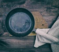 sartén redonda negra con mango de madera y servilleta de cocina de lino gris sobre una mesa de madera marrón foto