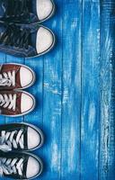 Three pairs of old sneakers on blue worn wooden background photo