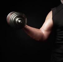 hand of a man with big biceps holds a steel type-setting dumbbell, low key photo