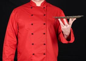 chef con uniforme rojo sostiene en su mano izquierda un plato redondo de cobre vacío foto