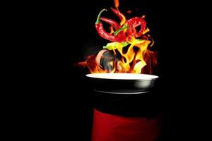 chef in a black uniform holds a round pan and throws up red and green whole chili peppers photo
