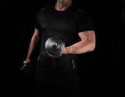 man in black clothes holds steel dumbbells in his hands, his muscles are tense photo