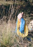 male hand of a Ukrainian army soldier raised up among the grass and holds the state yellow-blue flag photo