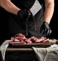 chef con guantes de látex negros sostiene un cuchillo grande y corta en trozos carne de conejo cruda foto