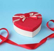 closed red heart-shaped gift box with a bow on a blue background photo