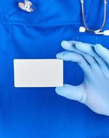 médico masculino con guantes de látex azules sostiene una tarjeta de visita de papel blanco en blanco foto
