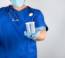 doctor in blue uniform and latex gloves is holding an empty plastic container for taking urine samples photo