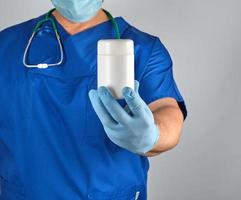 doctor in blue uniform is holding a plastic white jar with pills photo