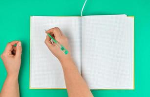 female hand holding pen, near  blank open notebook in a cell photo