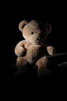 old brown teddy bear is sitting on a wooden surface photo