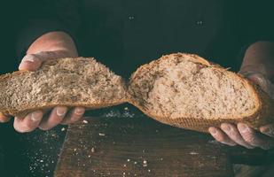 chef in black uniform holds in his hands half of broken off crusty bread baked from rye flour photo