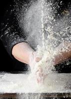 chef in black uniform sprinkles white wheat flour in different directions photo