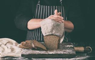 chef con uniforme negro pan de centeno horneado en rodajas sobre una tabla de madera marrón espolvoreada con harina blanca foto