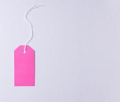 Empty pink cardboard tag on a white rope, pink background. Price tag template photo