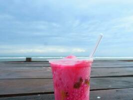 Es Podeng or Pink drink on a wooden table with Beach Background, Indonesia photo