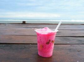 Es Podeng or Pink drink on a wooden table with Beach Background, Indonesia photo