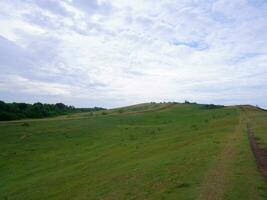 Green grass field on small hills and blue sky with clouds and dirt trails in Indonesia photo