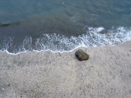 View of the shoreline from above, white waves, beach sand, clear water and rocks. Panoramic view. Beautiful beaches photo