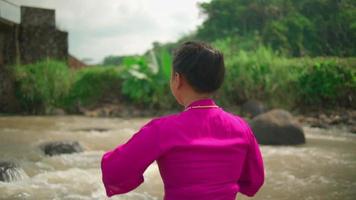 Asian woman takes off the jewelry from her neck while wearing a pink dress and makeup near the river in the village video