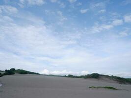 Sand Dunes hill white beach Green grass, and bright blue sky on tropical Indonesian beach, panoramic view photo