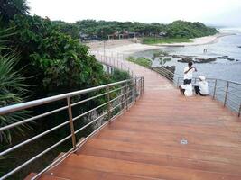 garut, indonesia, diciembre 12,2022 personas sentadas o recreativas en la carretera o puente o escaleras de madera en la playa, vista del puente de la playa en sayang heulang indonesia foto