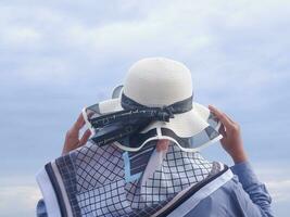 Back of the woman in the hat on the tropical beach who is looking at the sky and the sea while holding her hat photo