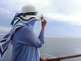 Back of the woman in the hat on the tropical beach who is looking at the sky and the sea while holding her hat photo