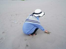 Back of the woman in the hat who was sitting and playing beach sand, the view of the sand photo